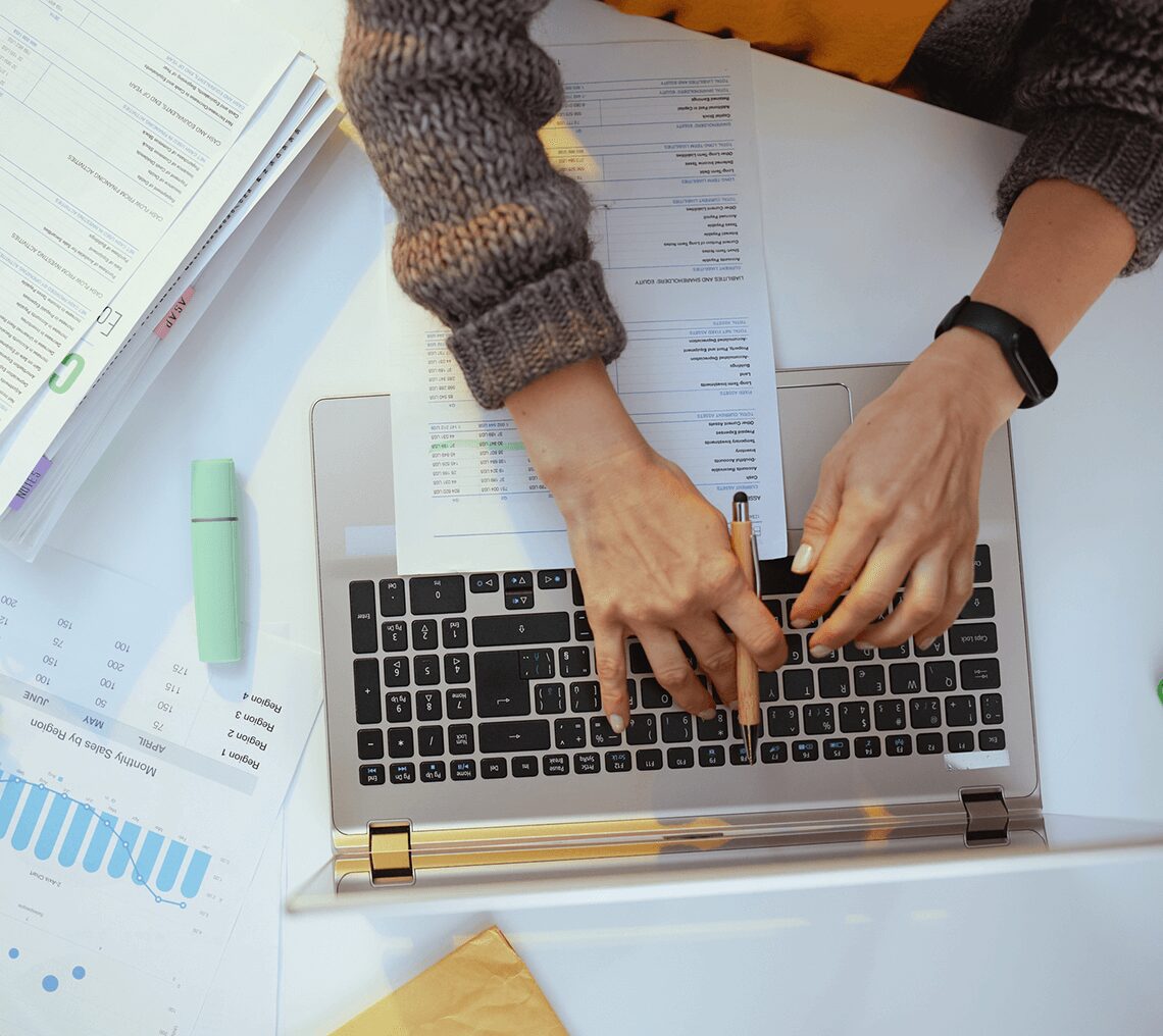Person typing on laptop with documents around.